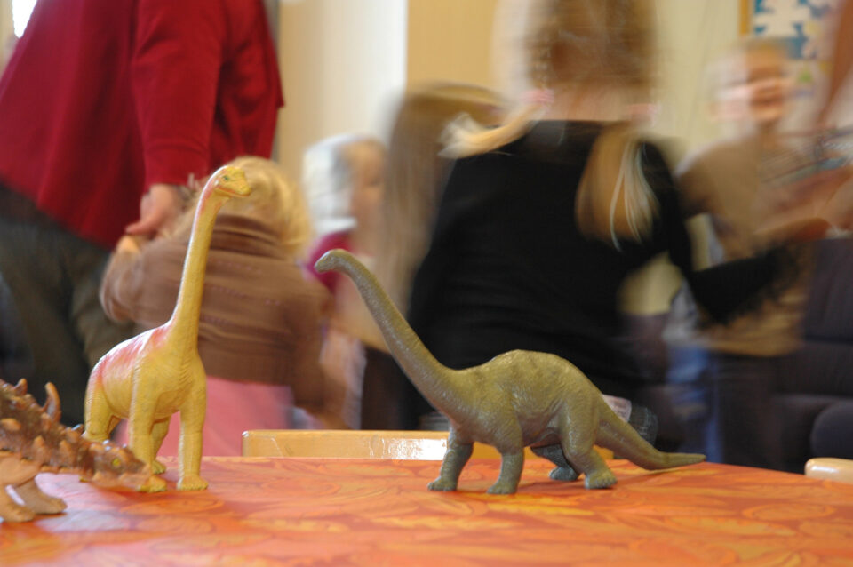 Dinosaurusleluja pöydällä, taustalla lapsia